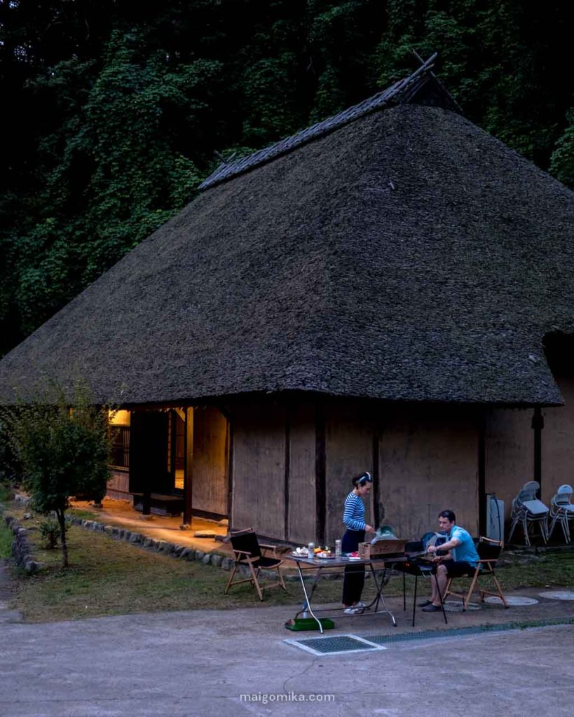 two people cooking bbq in front of traditional japanese house with cedar roof in Japan