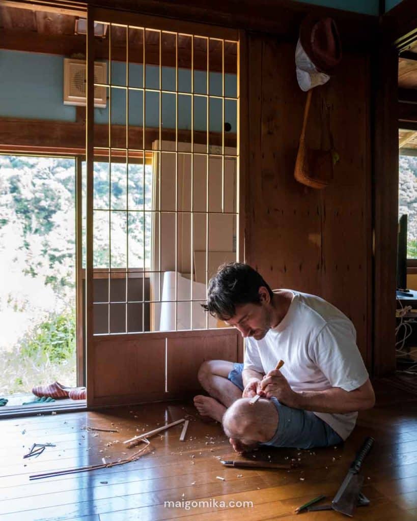 man sitting on floor of Japanese house with wood chips around him while fixing shoji screen repair