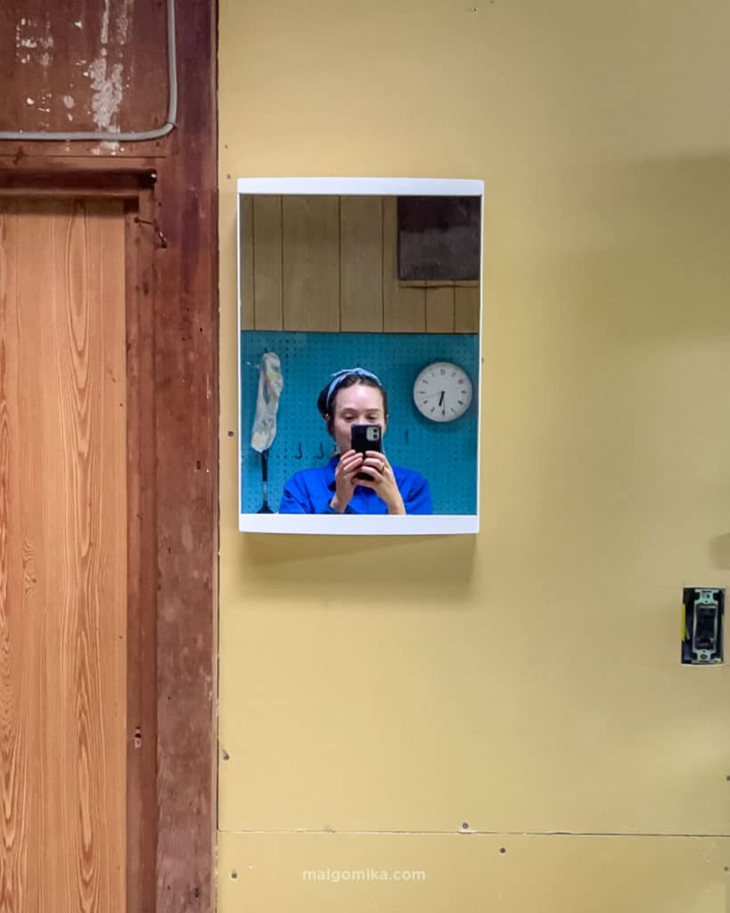 maigomika (girl) in blue coveralls taking picture of self with iphone in newly installed vanity