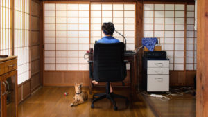 woman sitting at desk with japanese screen doors in background and small dog in corner