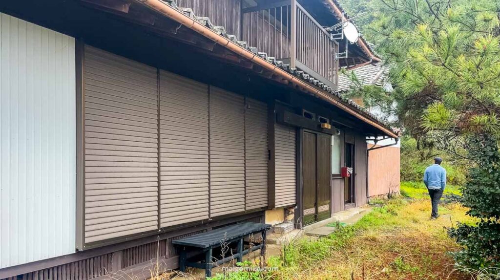 shuttered doors on traditional Japanese house, with man in blue sweater walking past