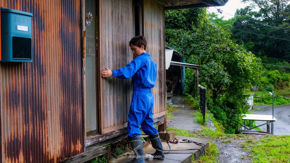 Woman in blue setting up amado storm doors on a traditional Japanese house, one of the many steps for typhoon and other natural disaster preparation in Japan.