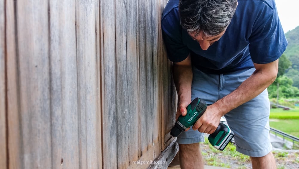 Man drilling screws into an amado, a Japanese style storm door, one of the many steps for typhoon and other natural disaster preparation in Japan.