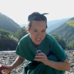 Maigo Mika, a woman wearing a green dress facing the camera with a microphone in hand, smiling